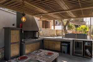 Een buitenkeuken met een ingebouwde barbecue, een eettafel met placemats en een hanglamp.