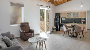 A spacious living area with a sofa, a round coffee table, and a dining table with chairs. A sliding glass door leads to an outdoor patio. - Countryside Villa with a Walk-in Free Form Pool (Rethymno)