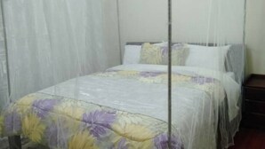 A single bed with a floral bedspread, a white mosquito net, and a wooden nightstand. - Stylish 2BR Kilimani Retreat | Lift, Fast WiFi & Family-Friendly Comfort (Nairobi)