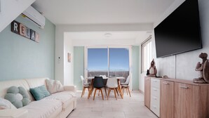 Una sala de estar moderna con un sofá, una mesa de comedor, sillas y un televisor montado en la pared.
