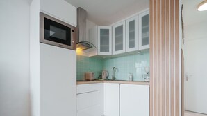 Una cocina compacta con armarios blancos, microondas, tostadora y cafetera.