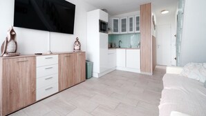 Una sala de estar moderna y minimalista con un televisor de pantalla plana, un mueble de madera y una cama con una colcha estampada.