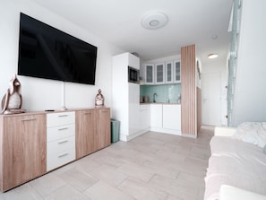 Un salon moderne et minimaliste, doté d’un téléviseur à écran plat, d’un meuble en bois et d’un lit recouvert d’une couvre-lit à motifs.