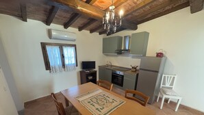 A compact kitchen with a dining area, featuring a wooden table, chairs, a TV, and a refrigerator. - Apartment located within an Agriturismo with swimming pool in Maremma n.2 (Scansano)