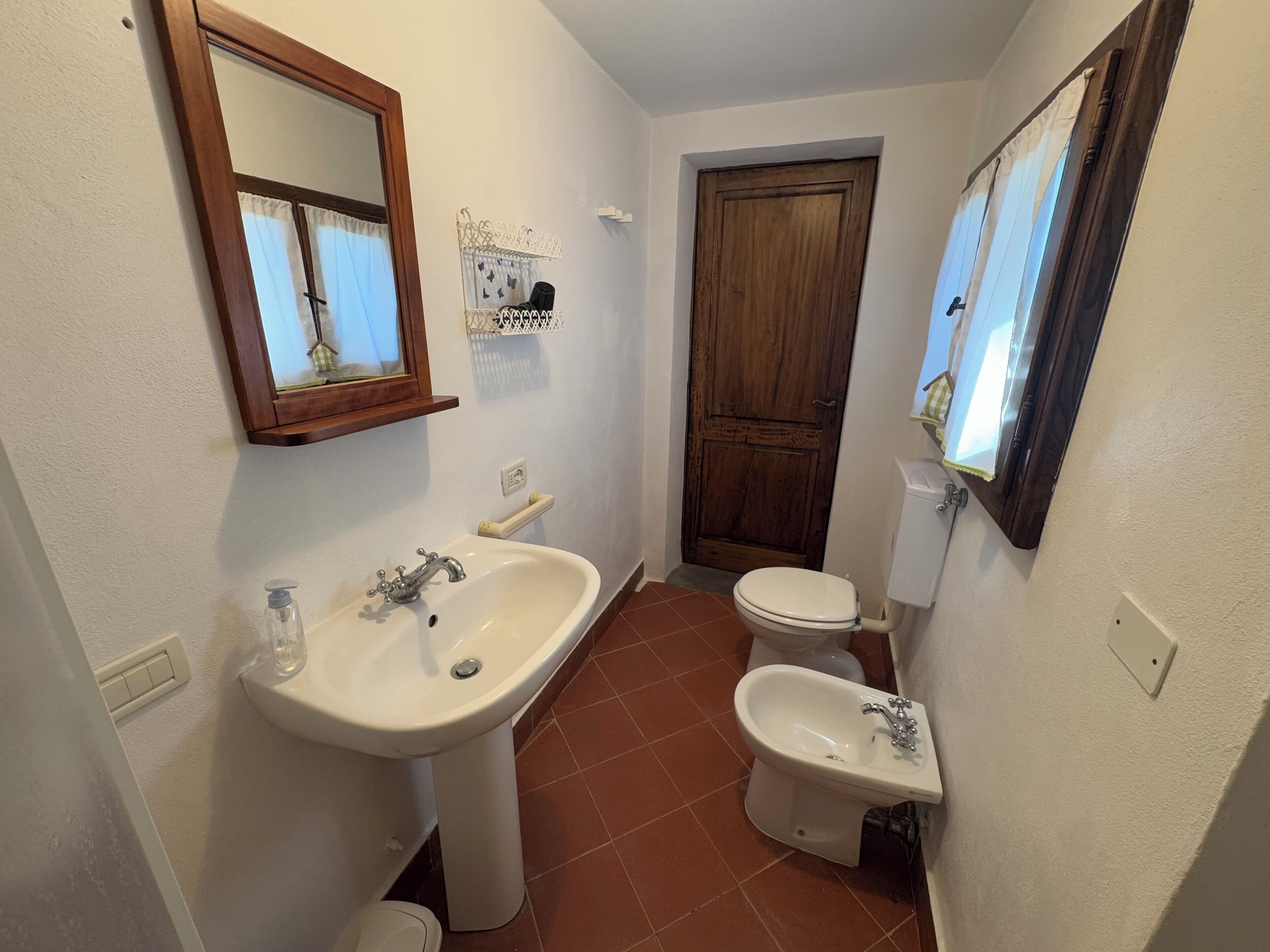 A compact bathroom with a sink, bidet, toilet, and a wooden door.