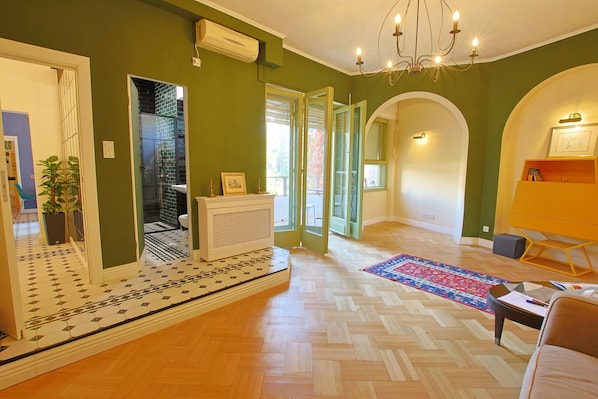 A spacious living area with a herringbone floor, a large mirror, and a chandelier.