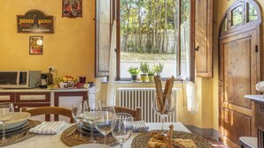 Ein Essbereich mit einem Tisch für vier Personen, ein Fenster mit Blick auf Bäume und eine Küchenzeile mit einer Mikrowelle und einem Kühlschrank.