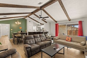 A spacious living area with a high ceiling, exposed wooden beams, a dining area, and a kitchen. - Incredible Location | King Bed | Sleeps 14 (San Antonio)