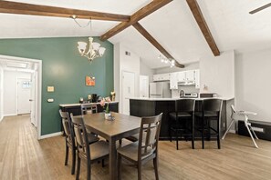 Ein Essbereich mit Holztisch und -stühlen, einer Chandelierleuchtre und einer Küche im Hintergrund.