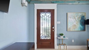 A room with a wooden door, a small white table with a plant, and a painting on the wall. - The Stafford Cottage-Close to The Pearl & Downtown (San Antonio)