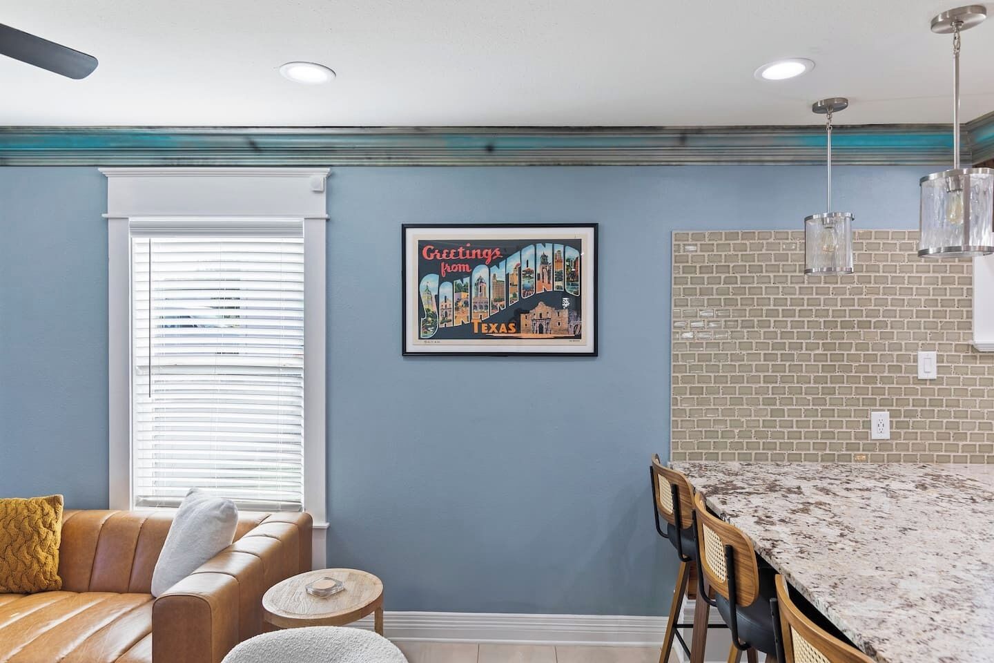 Eine moderne Küche mit Granit Arbeitsplatte, einem Essbereich mit Holztisch und -stühlen, einer blauen Akzentwand und einem gerahmten Stadtbild-Poster.