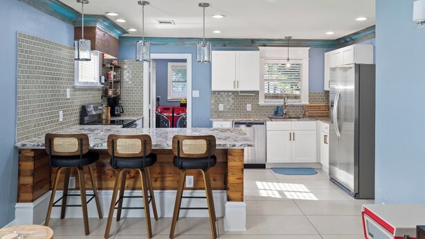 A modern kitchen with a central island, bar stools, and a stainless steel refrigerator. - The Stafford Cottage-Close to The Pearl & Downtown (San Antonio)
