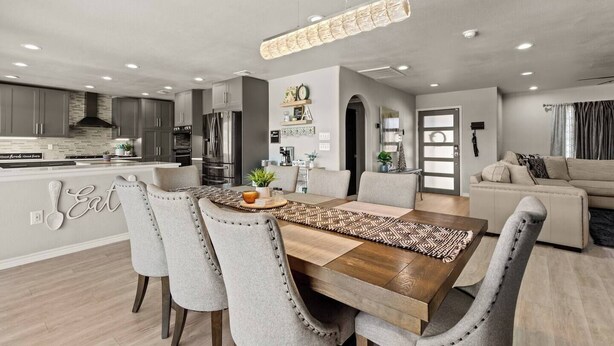 A modern kitchen with stainless steel appliances, a dining area with a wooden table and grey upholstered chairs, and a living room with a sofa and a large window. - Great Location-Huge Pool | Sleeps 14 | 2 King Beds (San Antonio)