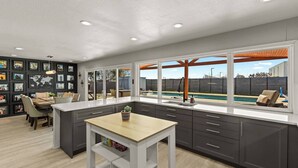 A modern kitchen with a large island, dark cabinetry, and a view of a backyard with a pool. - Great Location-Huge Pool | Sleeps 14 | 2 King Beds (San Antonio)