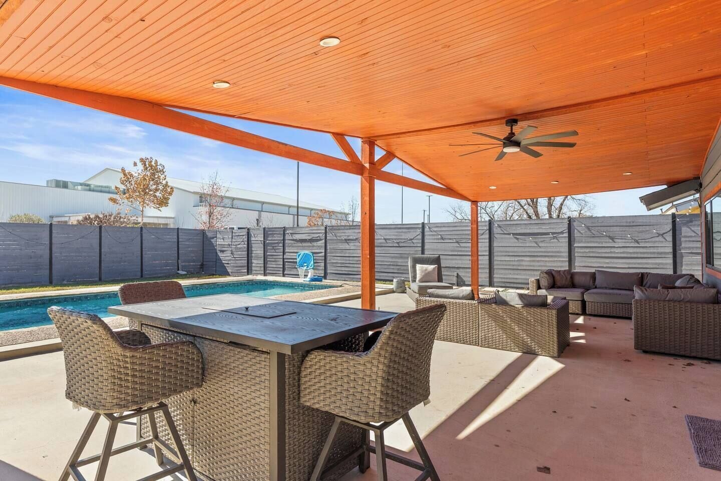 Um pátio externo com piscina, móveis de vime e ventilador de teto.