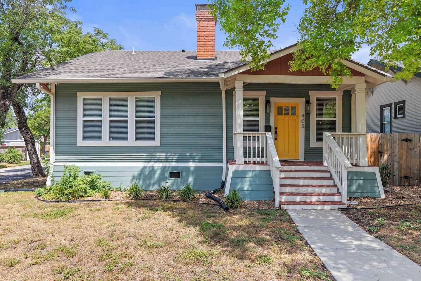 A single-story house with a front porch, a yellow door, and a chimney.