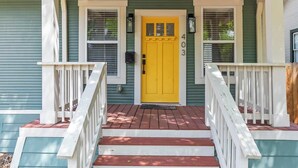 Une maison avec une porte d’entrée jaune, des balustrades blanches et un porche avec des marches.
