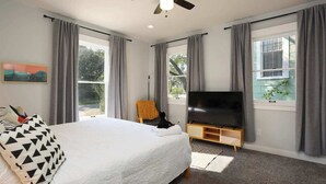 Une chambre à coucher avec un grand lit, un téléviseur posé sur un meuble en bois et un ventilateur de plafond.