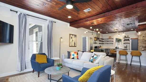 Un salon moderne avec un canapé, deux fauteuils, une table basse et une cuisine en arrière-plan.