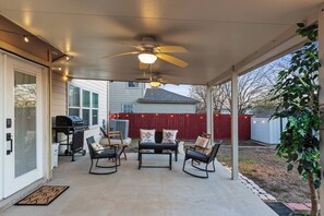 Eine überdachte Terrasse mit Deckenventilator, Gartenmöbeln und einem Grill.