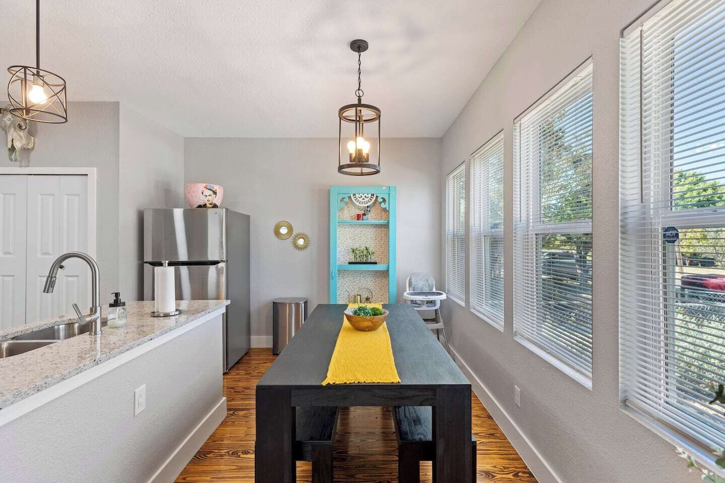Une cuisine équipée d’une table à manger, d’un réfrigérateur, d’un évier et d’une fenêtre avec des stores.