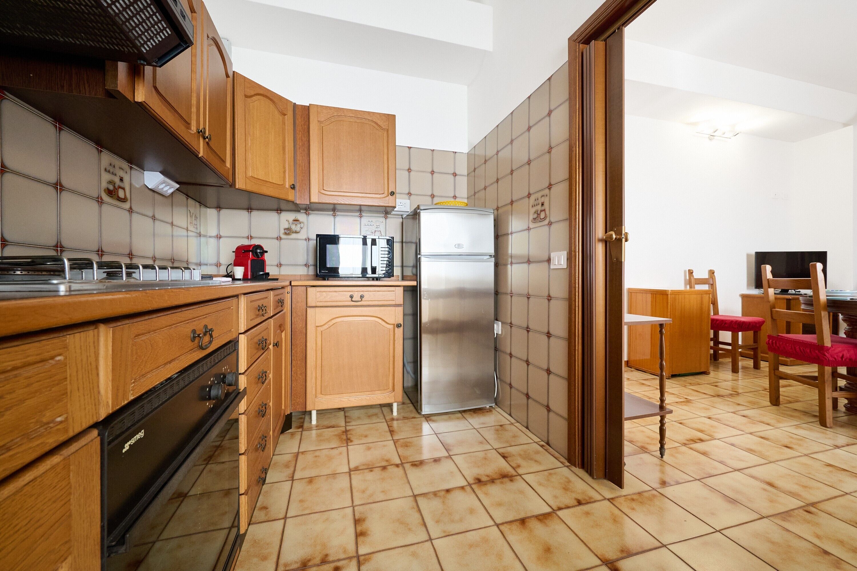 A compact kitchen with wooden cabinets, a stainless steel refrigerator, a microwave, and a coffee maker.