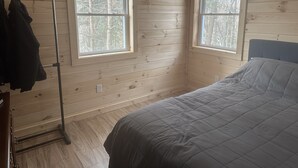 Een kamer met houten wanden, twee ramen, een bed en een kapstok.