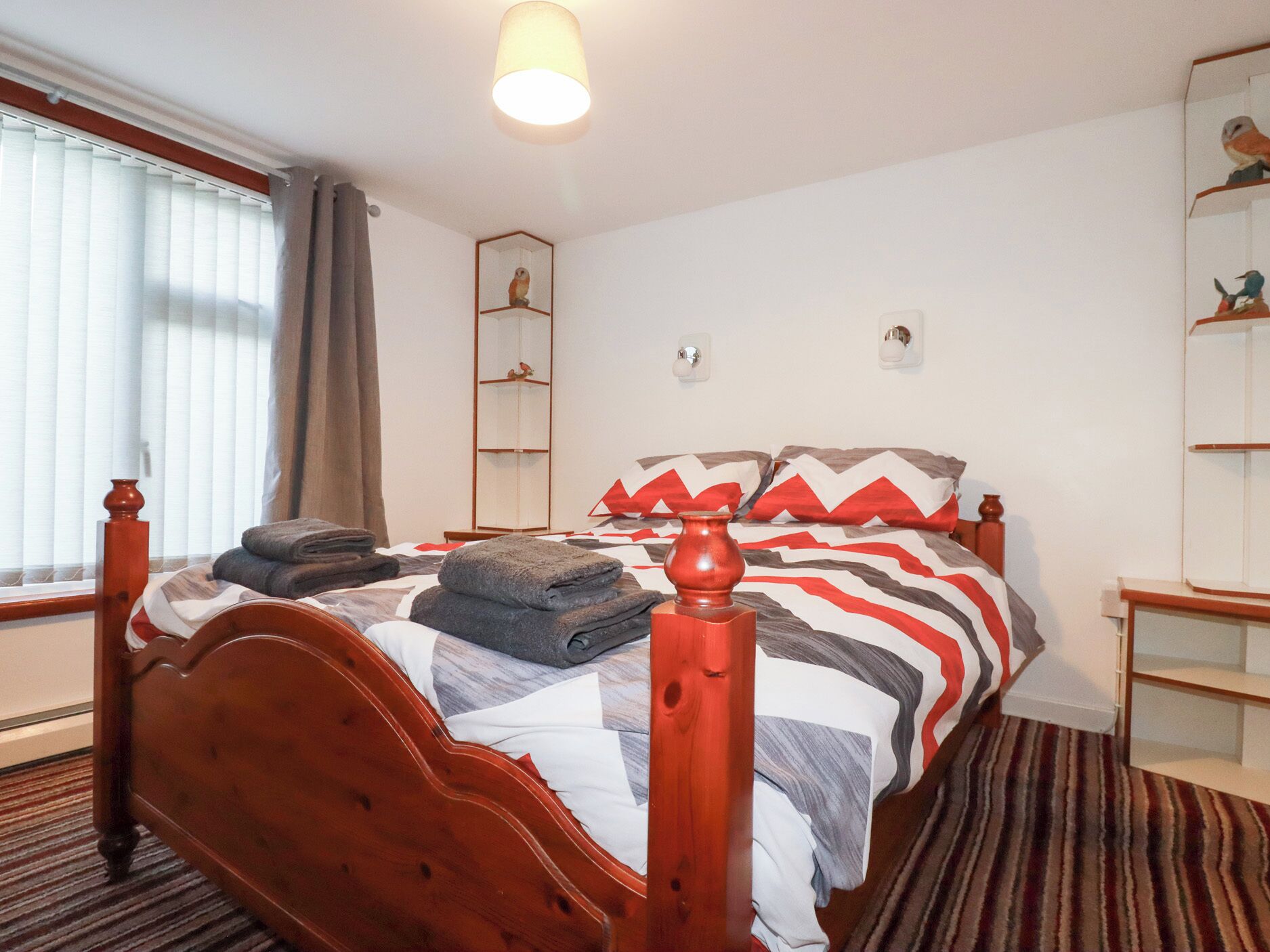 A neatly made bed with a striped bedspread, a wooden headboard, and a bedside table with a lamp.