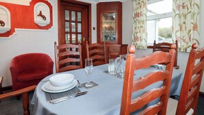 Uma sala de jantar com mesa posta para quatro pessoas, cadeiras de madeira, uma poltrona vermelha e um objeto decorativo na parede.