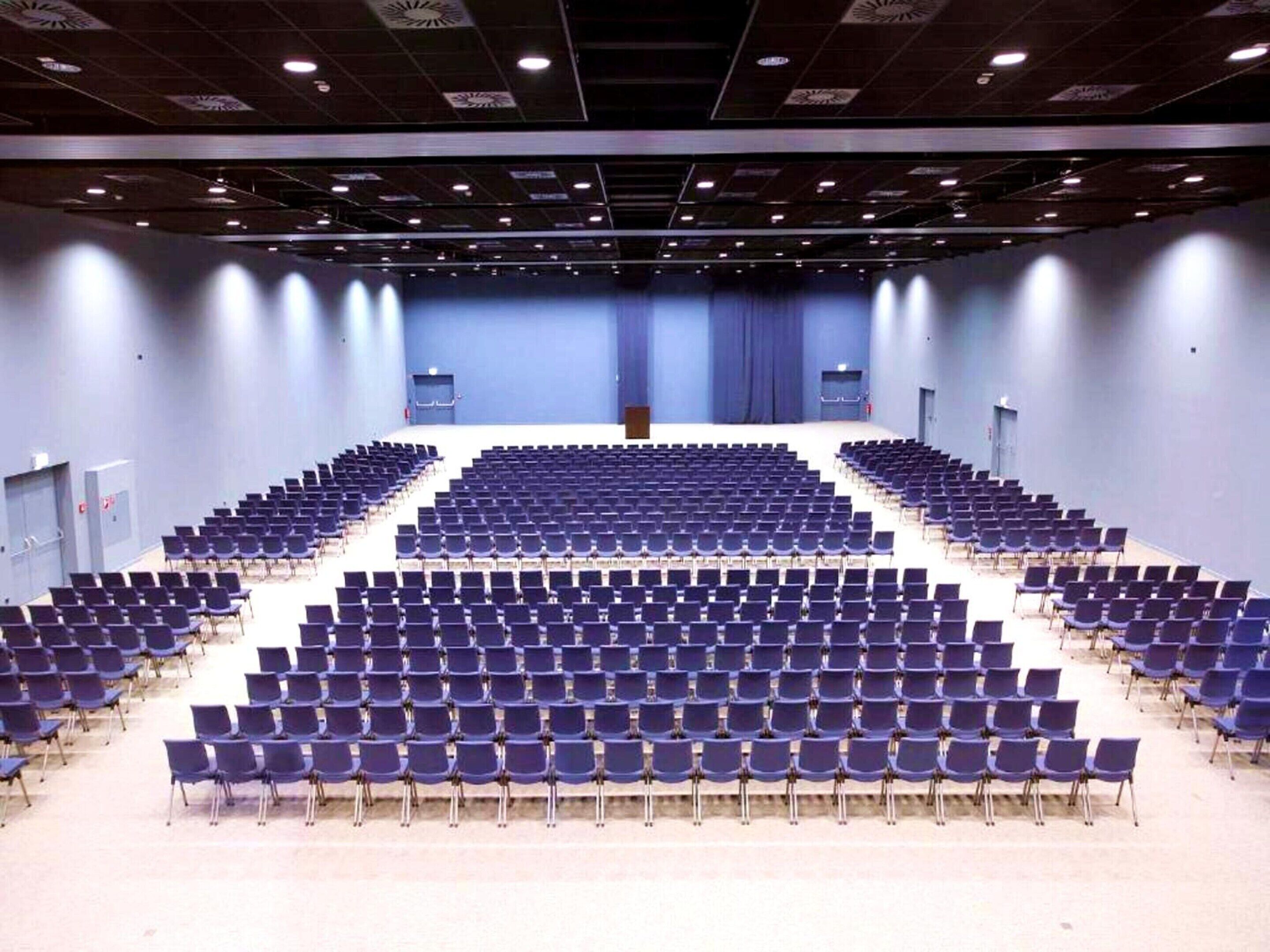 A large, empty auditorium with rows of blue chairs and a stage at the front.