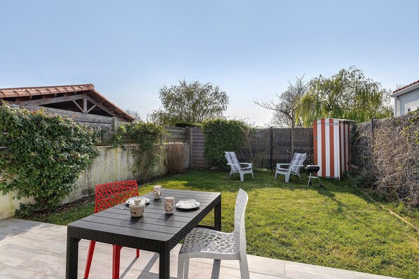 Eine Terrasse mit Tisch und Stühlen, eine kleine Gartenhütte und ein Rasen.