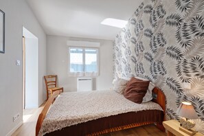 A bedroom with a bed, a chair, a nightstand, a lamp, a window, and a wall with a leaf pattern.
