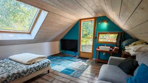 A cozy attic room with a sloped ceiling, a bed with a patterned bedspread, a sofa with cushions, a small table with a sink, and a television.