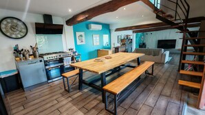 A modern kitchen with wooden flooring, a dining table with benches, a staircase, and a living area with a sofa.