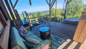 A covered outdoor seating area with a cushioned bench, a fire pit, and a view of the landscape.