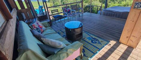 A covered outdoor seating area with a cushioned bench, a fire pit, and a view of the landscape.
