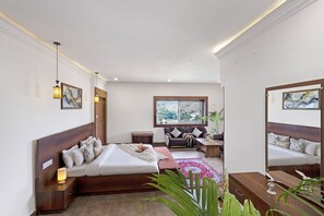 Un dormitorio moderno con una cama grande, un sofá, una mesita y un ventanal con vistas a la vegetación.