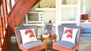 A staircase with wooden railings, two armchairs with red palm print cushions, a small round table with a woven rug, and a white shelving unit in the background. - Freddo's 2-4 persons with private pool (Capesterre-de-Marie-Galante)