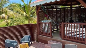 A poolside area with lounge chairs, a small table, and a covered seating area with a view of palm trees. - Freddo's 2-4 persons with private pool (Capesterre-de-Marie-Galante)