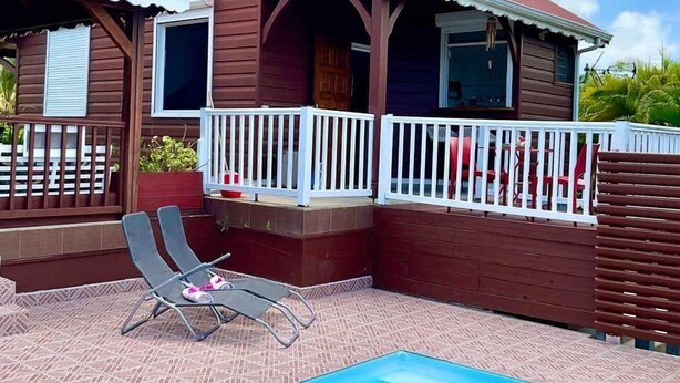 A two-story wooden house with a swimming pool, a covered patio, and a white fence. - Freddo's 2-4 persons with private pool (Capesterre-de-Marie-Galante)