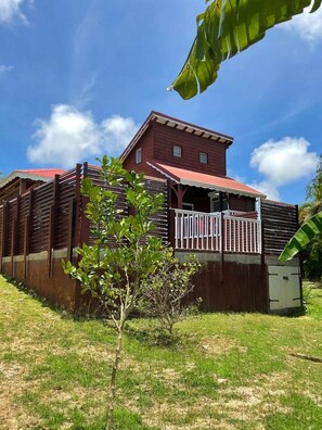 A red wooden building with a balcony, surrounded by grass and a few small trees. - Freddo's 2-4 persons with private pool (Capesterre-de-Marie-Galante)