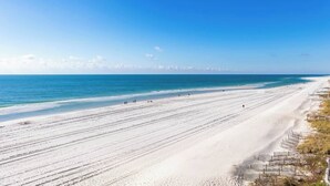 Una playa amplia y arenosa con cielo azul despejado y mar tranquilo.
