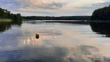 Ein ruhiger See mit einem gelben Gegenstand, der auf dem Wasser schwimmt, umgeben von dichten Bäumen und einem bewölkten Himmel.