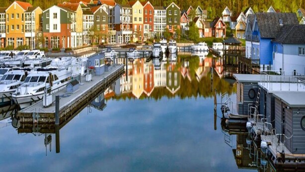 A marina with boats docked, a row of colorful houses, and a calm water surface reflecting the buildings. - Sunday Resort Marina 3-bedroom Apartment (Rheinsberg)