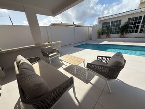 En udendørs patio med pool, to sofaer, et bord og plantekasser.