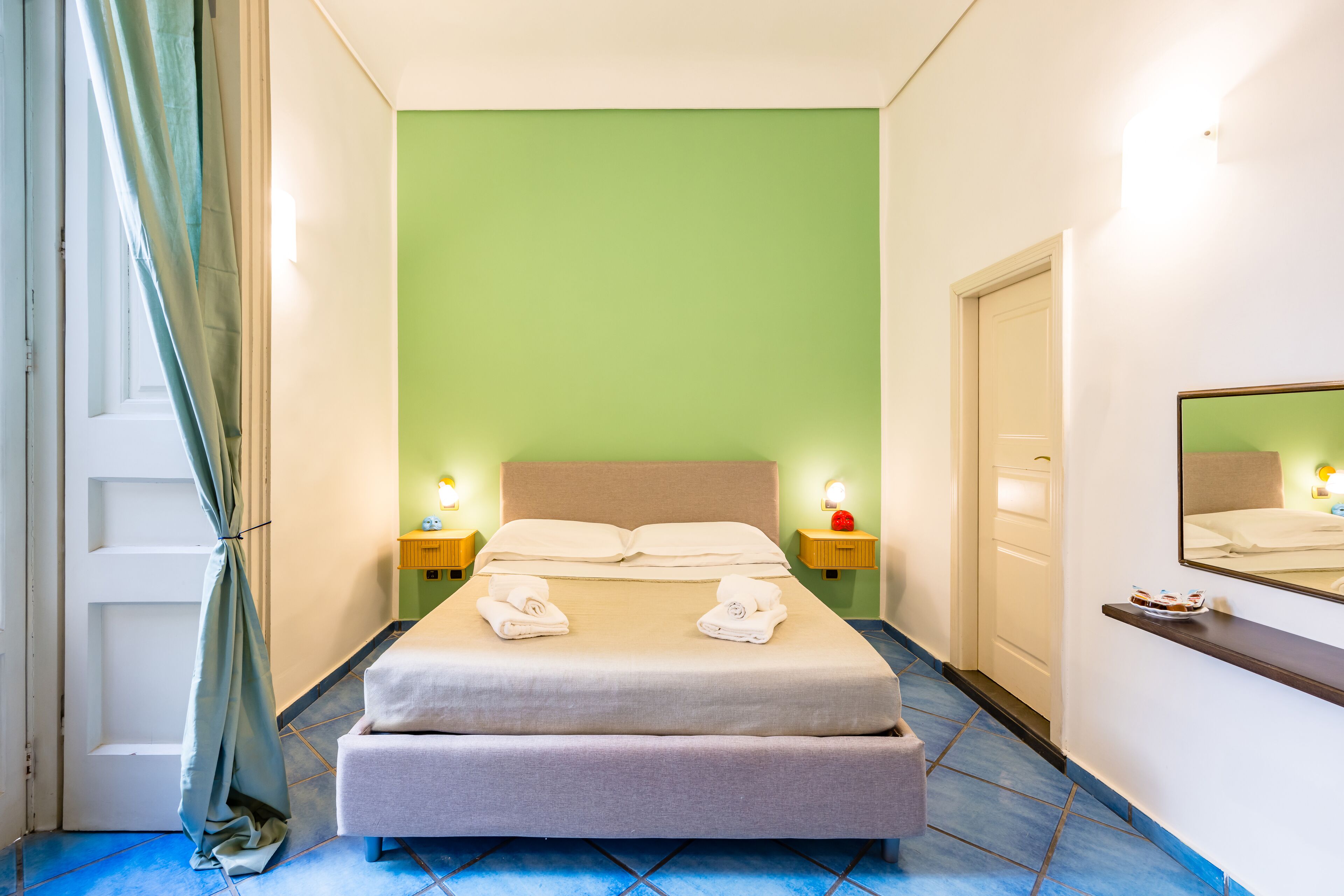 Een hotelkamer met een bed, twee nachtkastjes met lampen, een spiegel en een deur.
