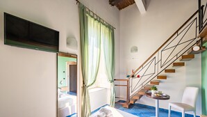 Ein modernes Hotelzimmer mit einem großen Flachbildfernseher, einer Treppe mit Holzbeschlägen, einem kleinen Tisch mit einer Pflanze und einem weißen Stuhl.