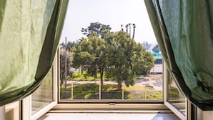Ein Fenster mit Blick auf einen Baum und ein eingezäuntes Areal.