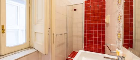 A bathroom with a white bathtub, a glass shower enclosure, and red-tiled walls.