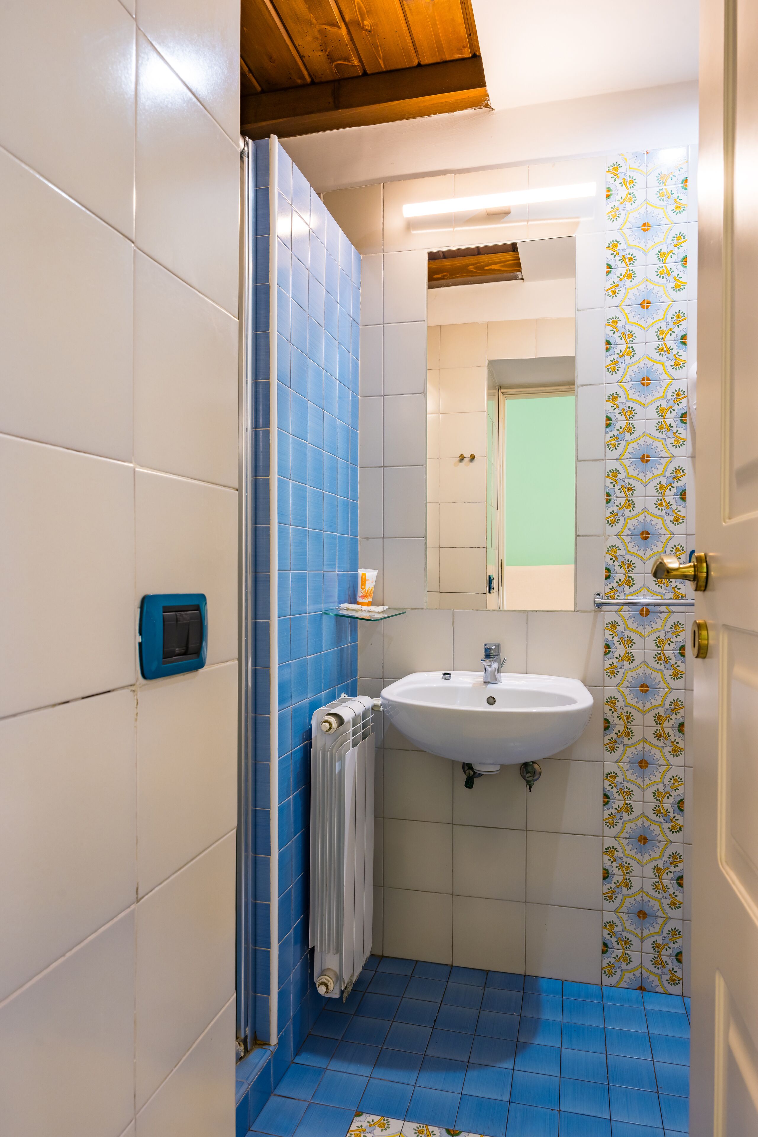 Une salle de bain avec des carreaux bleus, un lavabo blanc, un miroir et une douche.